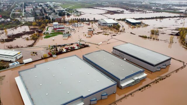 Aerial drone view of flooded industrial halls, warehouses, fields, and houses. Aftermath of devastating river flood and landslide. Catastrophic floods. Overflowing river, view from above.
