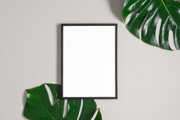 Empty black photo frame mockup and monstera leaf on gray background. Flat lay, top view, copy space