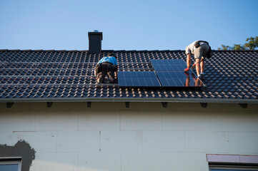 Two engineers on the house roof assemble photovoltaic panel.