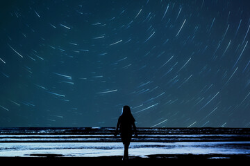 Girl stargazing at the beach the child is in silhouette looking at the night sky