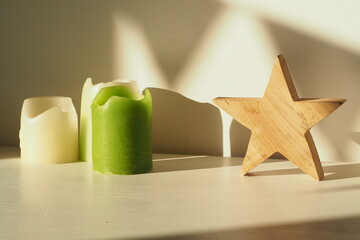Kompozycja ze świec i drewnianej gwiazdy na białym stole przy ścianie