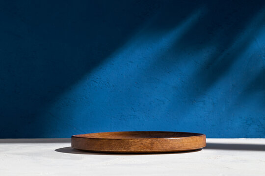 Cylinder shape wood podium with blue stucco wall and shadows. Front view. Mockup.	
