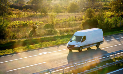 White modern delivery small shipment cargo courier van moving fast on motorway road to city urban...