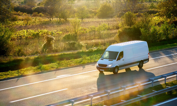 White modern delivery small shipment cargo courier van moving fast on motorway road to city urban suburb. 