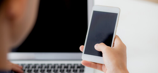 Hand of young man working with laptop computer and smartphone mockup on desk at home, notebook and phone display blank screen, freelance look message to internet, business and communication concept.
