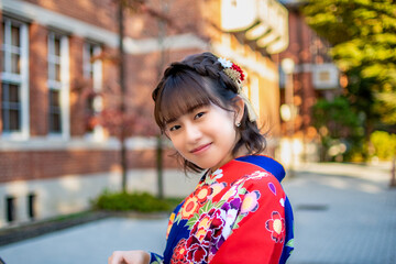 Female university student dressed in kimono at a university brick school building in Kyoto, Japan.