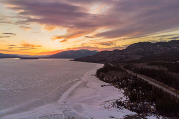 Drone, aerial view along the Alaska Highway in fall, autumn with stunning orange sunset over the frozen lake below. 