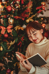 a young Woman in front of Christmas tree reading a book at home with x-mas decoration.