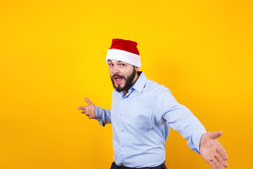latin man in christmas concept pointing fingers right with santa hat, having fun, smiling amazed on a yellow background in Mexico Latin America
