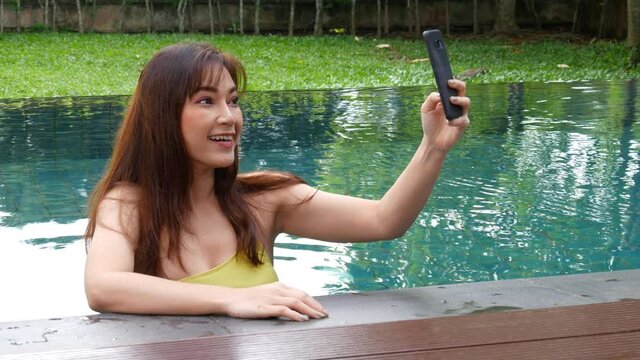 happy woman using smartphone to selfie a photo in the swimming pool