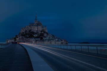 Obraz premium Le mont Saint Michel à l'heure bleue avec des phares de voitures en pose longue