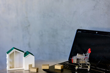 Shopping online and delivery concepts.
Miniature product package boxes in shopping cart and house models with laptop computer on wooden table.