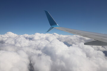 Obraz premium An airplane wing with a view of the bright blue sky and snow-white clouds illuminated by the sun