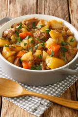 Traditional Scottish stovies consists of potatoes, meat, onions and carrots close up in the bowl on the table. Vertical