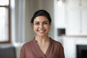 Head shot attractive young 30s Indian female with wide toothy smile posing on camera while standing...