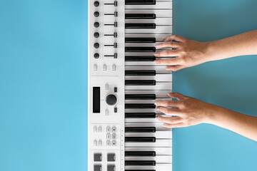 Female hands play musical keys on a blue background, top view.