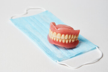 Fototapeta na wymiar Dental dentures and medical mask on white background