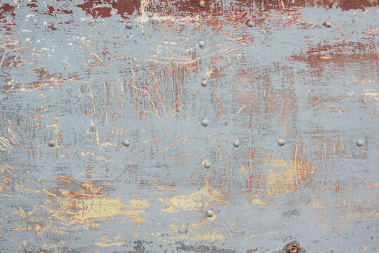 Fragment of a metal surface with rivets. Several layers of old paint of different colors are visible. Background. Texture.