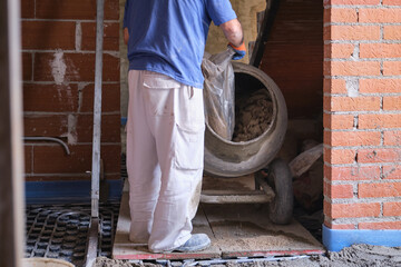 Construction worker loading a sandbag into the concrete mixer.