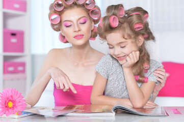 Mother and little daughter with hair curlers reading magazine