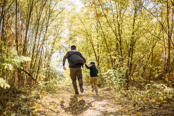 Fototapeta premium Father and son spend time in forest. Happy dad and child boy enjoying autumn time on vacation in a sunny park. Kids love parents affection and tenderness, lovely family.