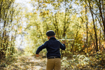 Young boy play with toy airplaine in hands. Happy Kid is playing in park outdoors