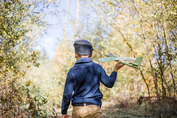 Young boy play with toy airplaine in hands. Happy Kid is playing in park outdoors