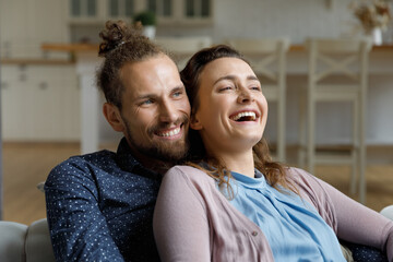 Obraz premium Happy affectionate young family couple man woman resting on cozy sofa, having fun watching smart television programs, entertaining enjoying leisure weekend time, daydreaming together at home.