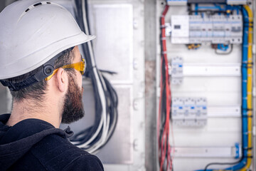 A male electrician works in a switchboard with an electrical connecting cable.