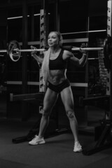 Fototapeta na wymiar A fit woman is squatting with a barbell near the squat rack in a gym.