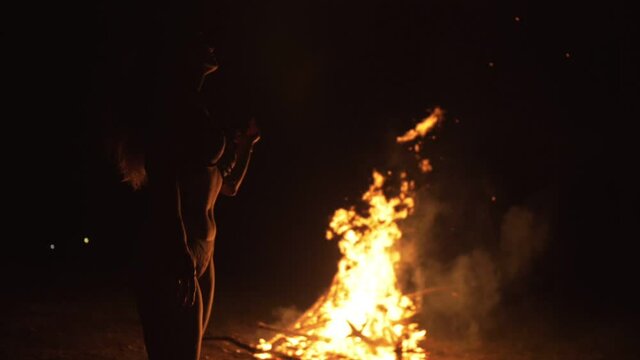 Silhouette of mystic woman in black background of fire fly flame, spark, of contour outline. Adult sexy of young girl witchcraft ceremony ritual dance in underclothes. Outdoor slow motion. Caucasian.