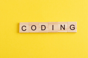 Word Coding made from wooden letters on yellow background. Concept of learning programming languages