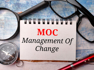 Magnifying glass,glasses,compass,pen and notebook with text MOC Management of Change on a wooden...