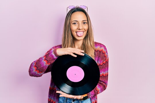 Beautiful hispanic woman wearing hippie style holding vinyl disc sticking tongue out happy with funny expression.