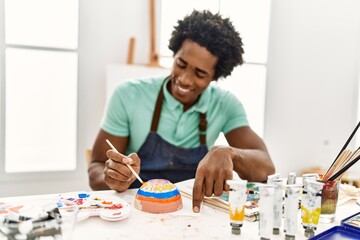 Young african american artist man painting ceramic at art studio.