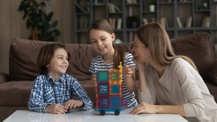 Loving mother with son and daughter playing with colorful plastic blocks, having fun at home together, smiling mom and kids engaged in creative educational activity, enjoying leisure time weekend
