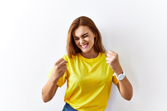 Young brunette woman standing over isolated background very happy and excited doing winner gesture with arms raised, smiling and screaming for success. celebration concept.
