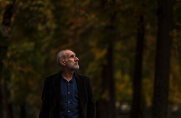 Portrait of adult man in suit in public park in autumn against green plants. Shot in Retiro Park, Madrid, Spain