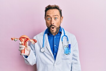 Middle age gynecologist man holding anatomical model of female genital organ scared and amazed with open mouth for surprise, disbelief face