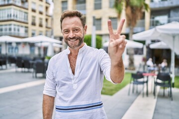 Middle age man outdoor at the city smiling looking to the camera showing fingers doing victory sign. number two.