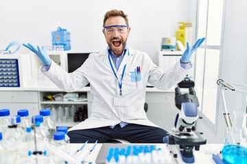 Middle age man working at scientist laboratory celebrating mad and crazy for success with arms...