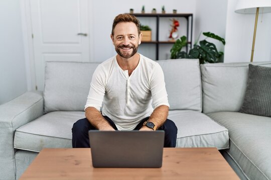 Middle age man using laptop at home with a happy and cool smile on face. lucky person.