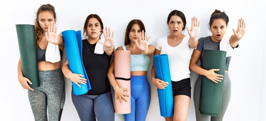 Obraz premium Group of women holding yoga mat standing over isolated background doing stop gesture with hands palms, angry and frustration expression