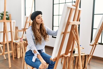 Young hispanic artist woman painting on canvas at art studio relaxed with serious expression on face. simple and natural looking at the camera.