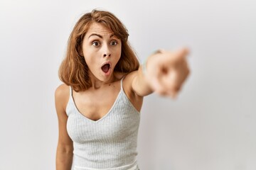 Beautiful caucasian woman standing over isolated background pointing with finger surprised ahead, open mouth amazed expression, something on the front