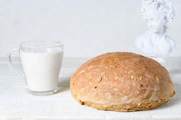 Homemade bread, cup of milk and sculpture on white rustic wooden table 