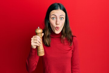 Young brunette woman black pepper grinder scared and amazed with open mouth for surprise, disbelief...
