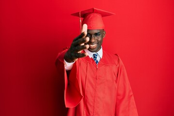 Young african american man wearing graduation cap and ceremony robe smiling friendly offering handshake as greeting and welcoming. successful business.