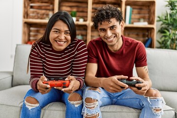 Young latin couple smiling happy playing video game sitting on the sofa at home.