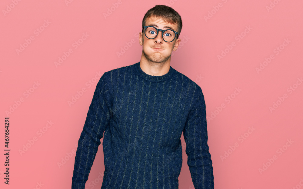 Poster young blond man wearing casual clothes and glasses puffing cheeks with funny face. mouth inflated wi